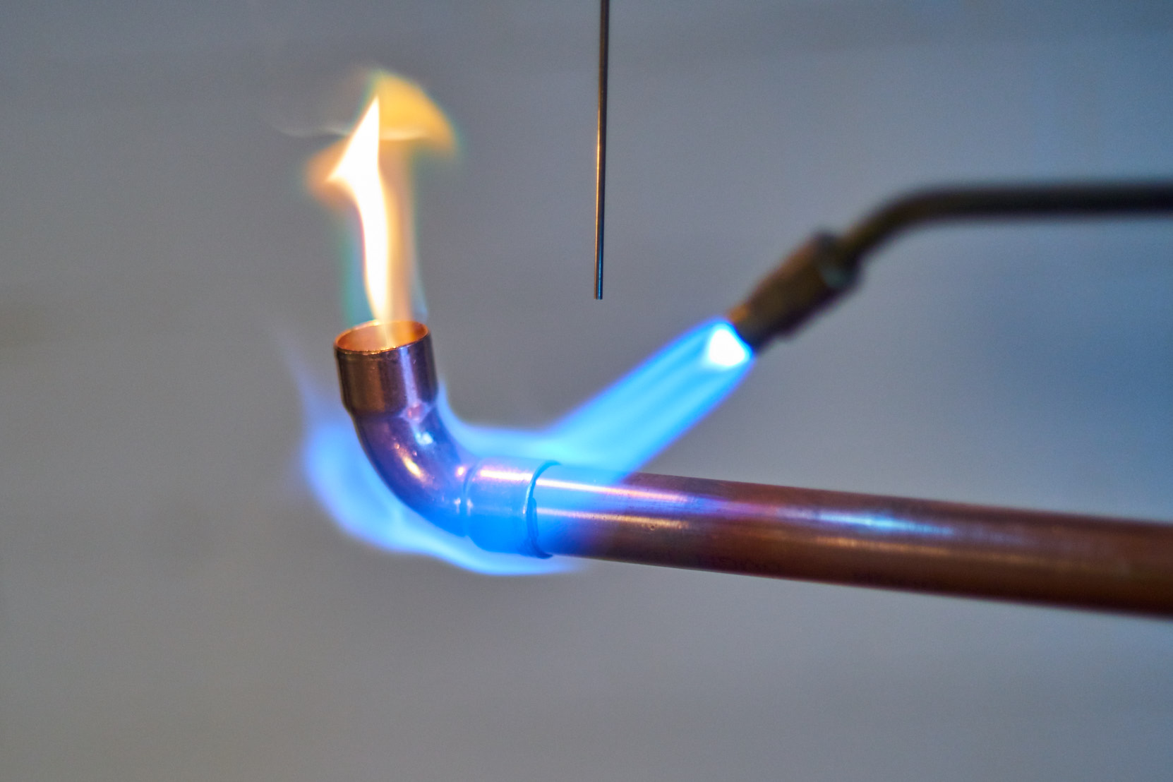 Kupfer-Eisenrohr der Marke RefHP® von SANHA® wird gelötet und stößt dabei rote Flamme aus